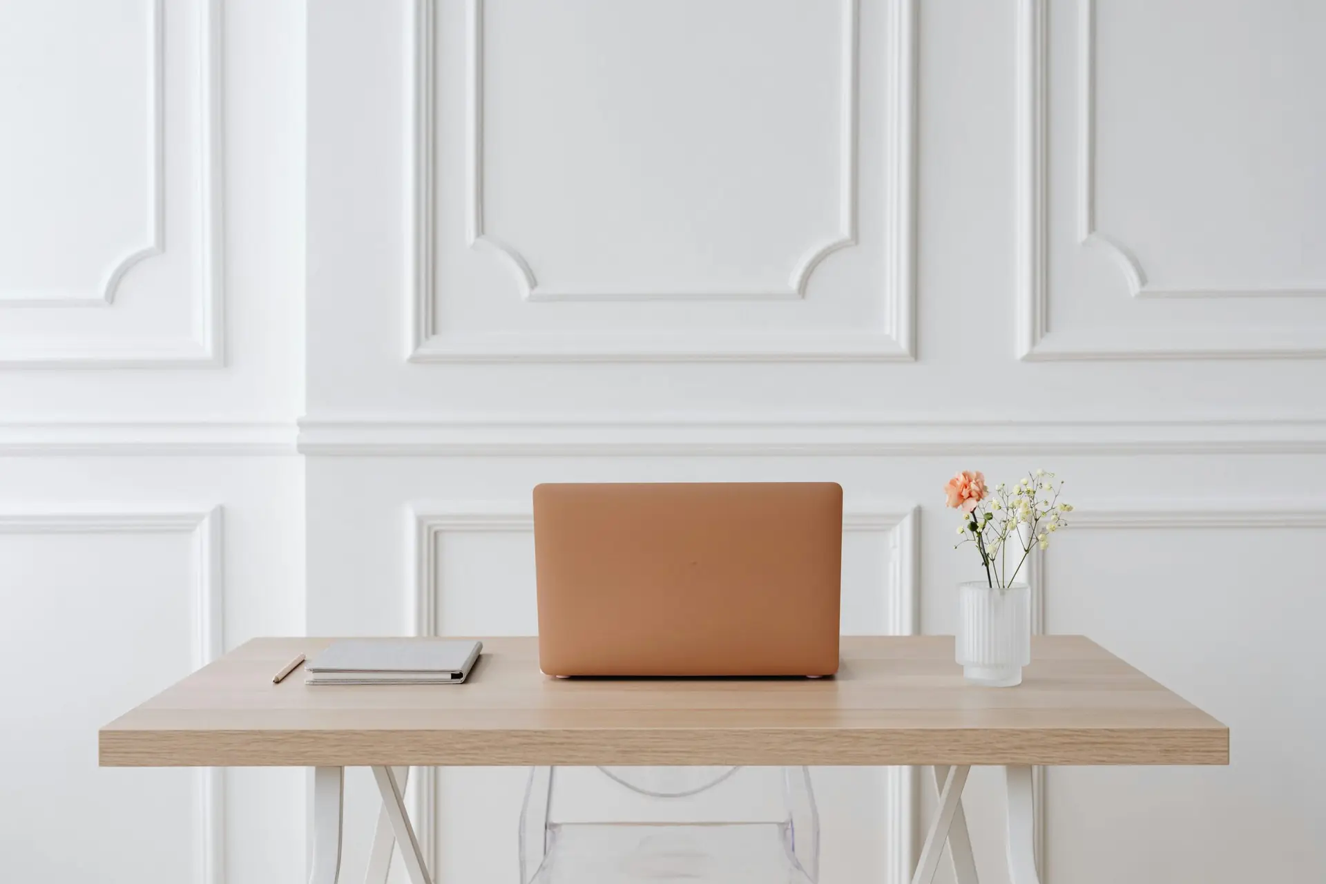 A serene workspace featuring a simple desk with a laptop, notebook, and a vase of flowers.